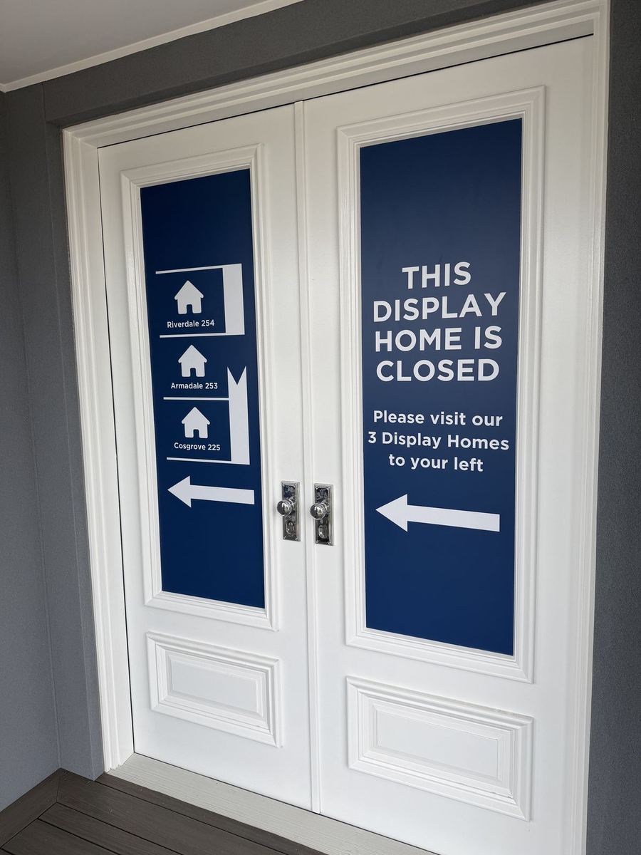 Blue directional graphics on white double doors pointing visitors left to three open display homes
