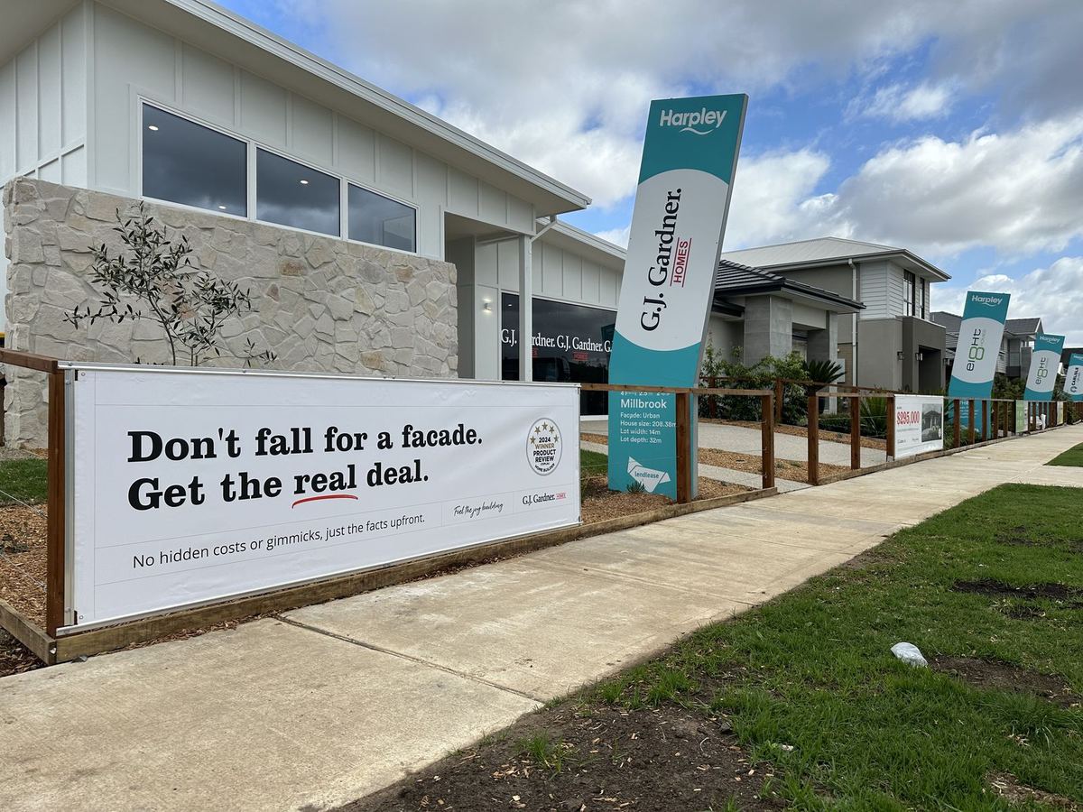 Display village street with a fence banner and tall pylon signs naming each display home