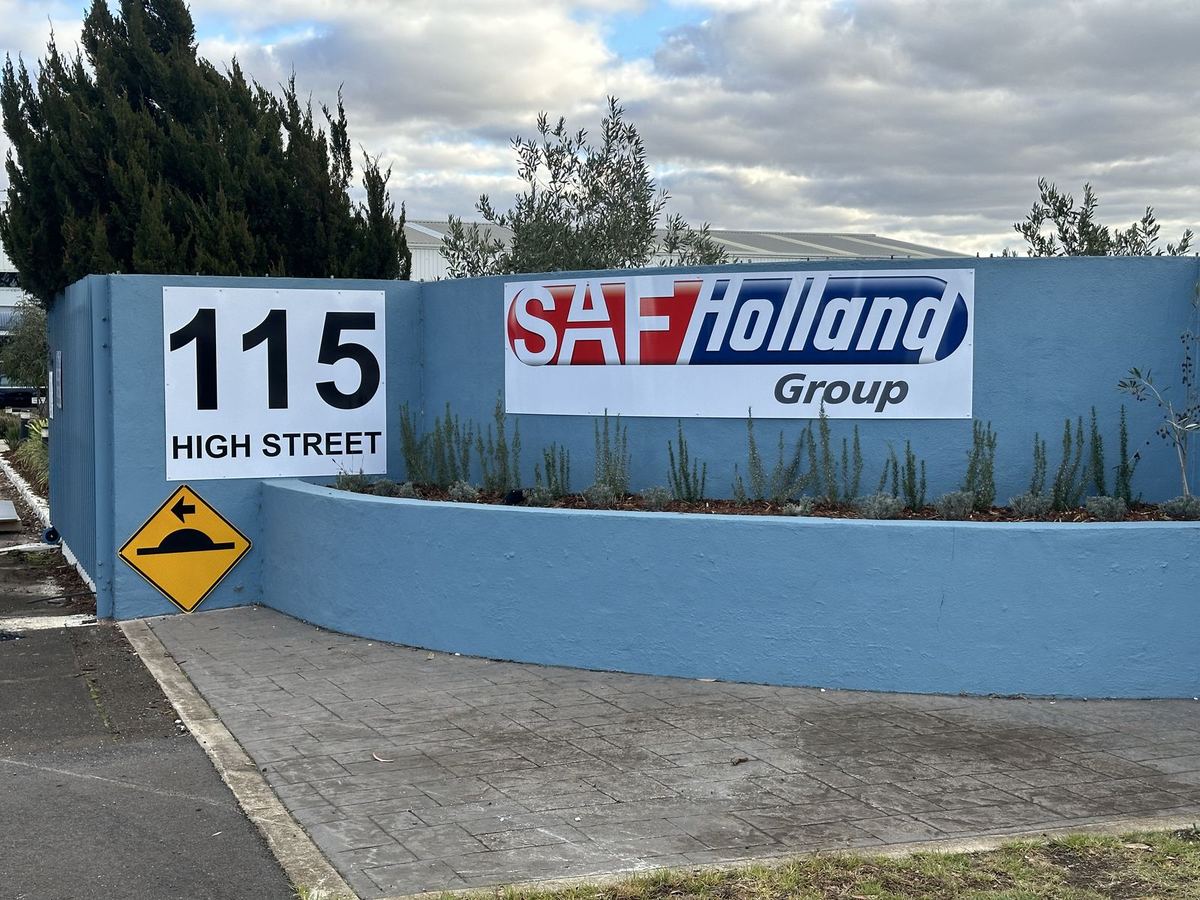 Company logo panel and street number sign mounted on a blue entrance wall at an industrial site