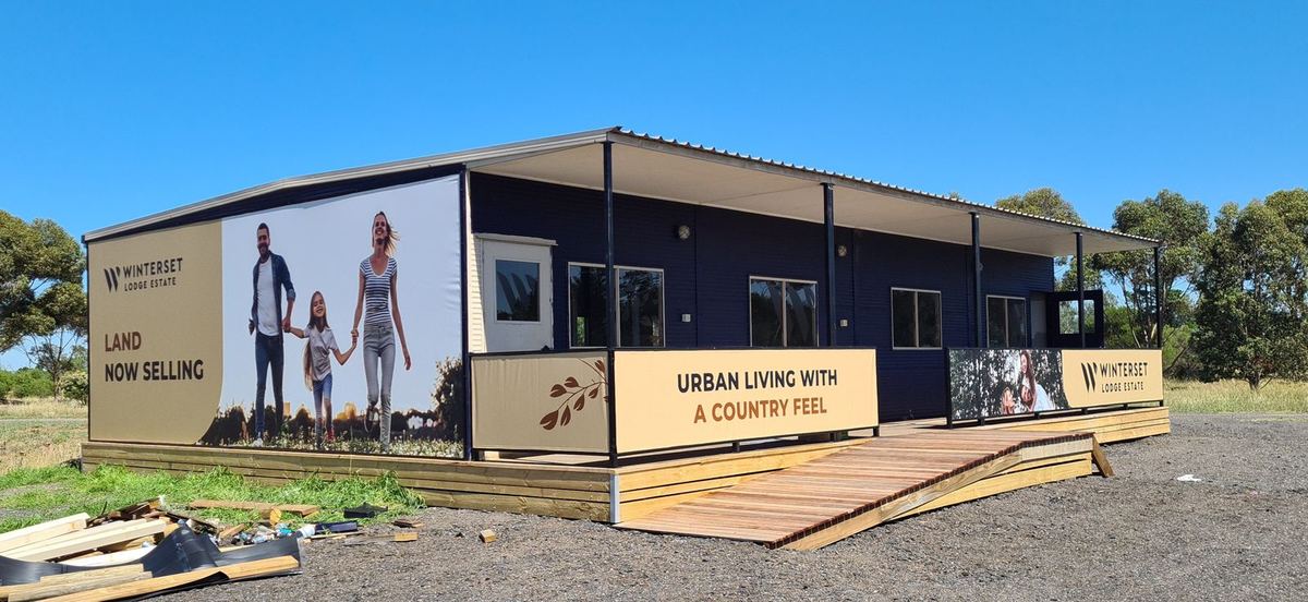 Winterset display suite with family imagery and Land Now Selling panels