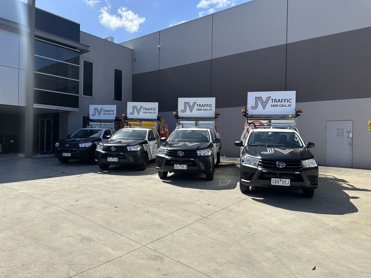 Four traffic management utes with matching partial wraps and roof-mounted signs outside a warehouse