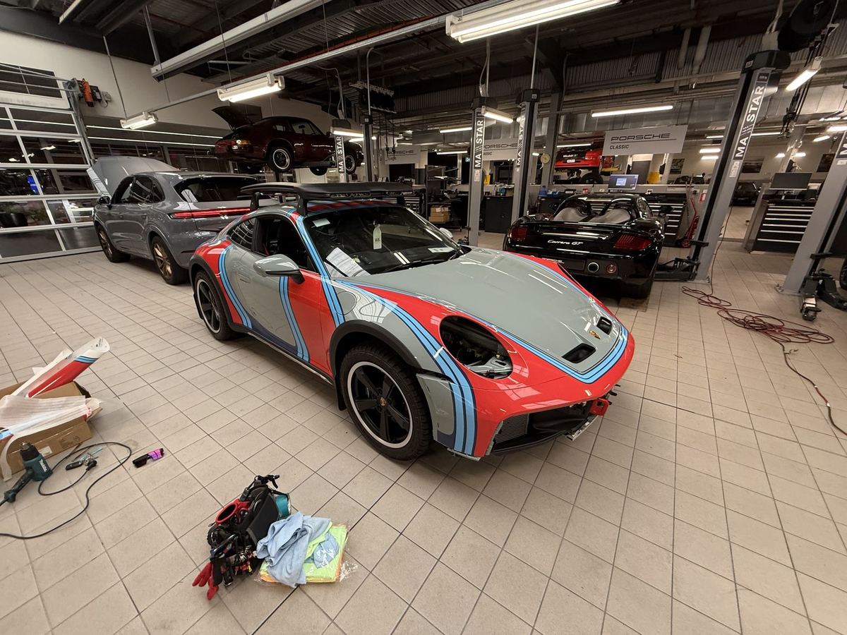 Livery wrap being fitted around the curved guards of a Porsche 911, heat gun on the workshop floor